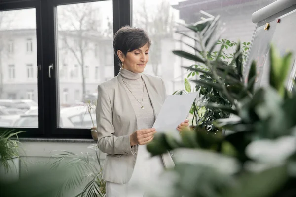 Positive middle aged businesswoman looking at document, working in modern office, project planning — Stock Photo