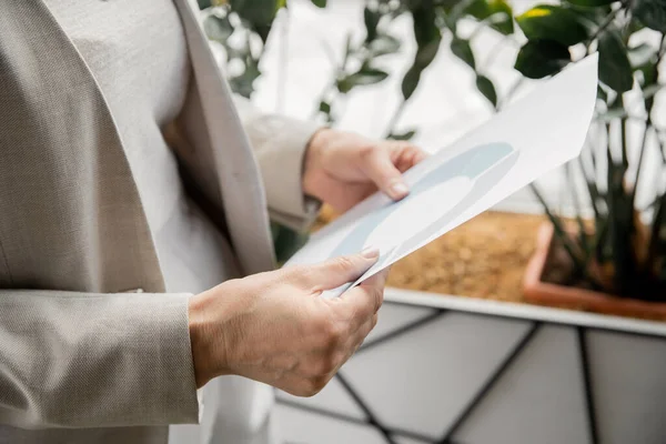 Cropped view of middle aged entrepreneur holding paper with infographics, successful business — Stock Photo