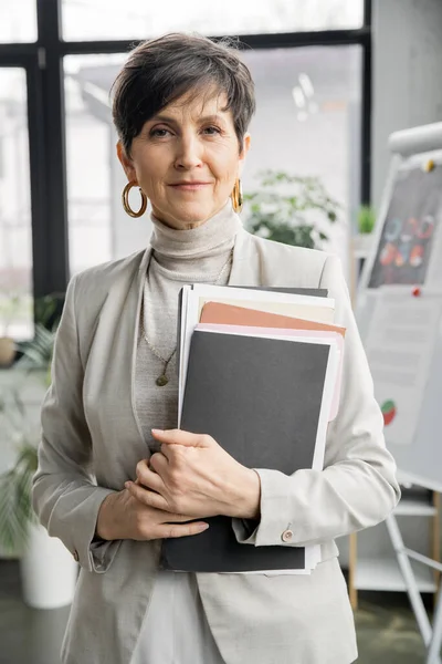Confident mature businesswoman looking at camera in office, folders, documents, portrait, headshot — Stock Photo