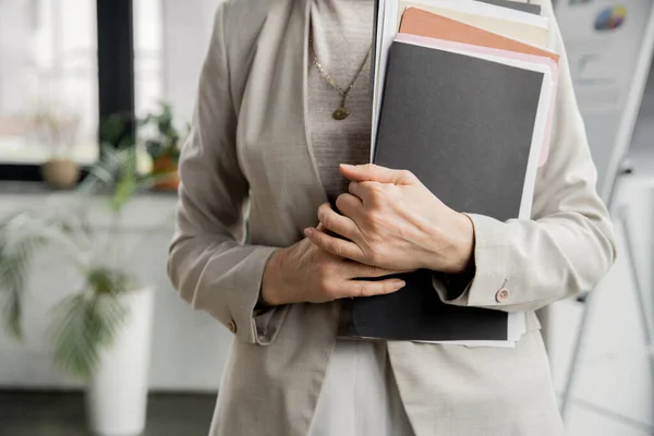 Cropped view of middle aged businesswoman standing with folders and documents in modern office — Stock Photo