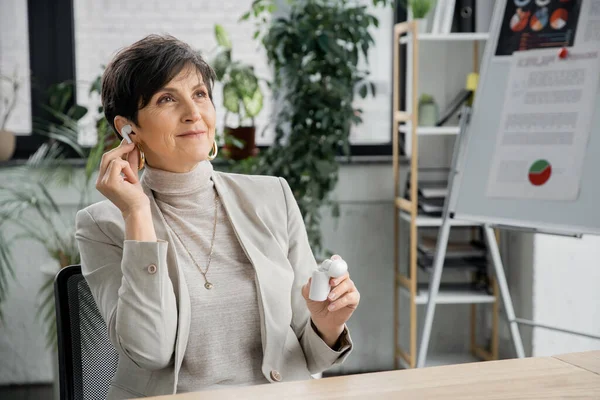 Mature businesswoman with earphone case listening music in office, entertainment, enjoyment — Stock Photo