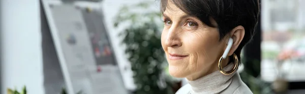 Smiling and dreamy middle aged businesswoman listening music in earphone and looking away, banner — Stock Photo