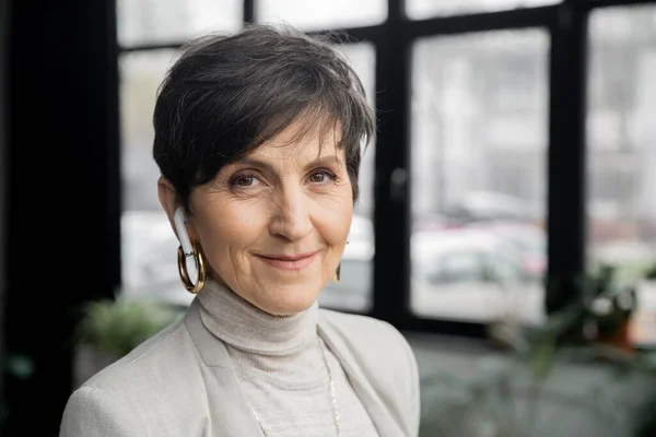 Happy and stylish middle aged businesswoman in wireless earphone looking at camera, headshot, banner — Stock Photo