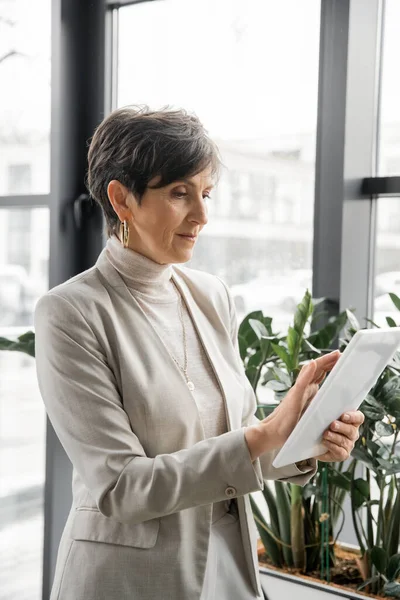 Зрелая женщина, корпоративный менеджер, работающий над цифровым планшетом в офисе, стратегическое планирование — стоковое фото
