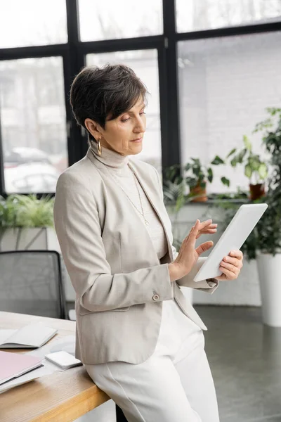 Thoughtful middle aged businesswoman with digital tablet standing at workplace in office — Stock Photo