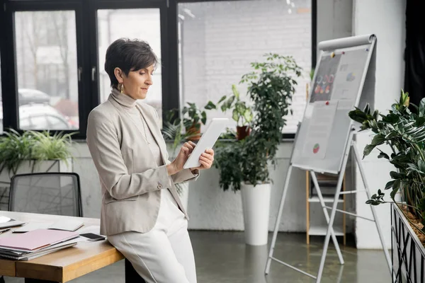 Femme mature entrepreneur avec tablette numérique documents soignés et tableau à feuilles mobiles avec infographies — Photo de stock