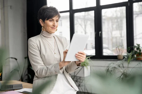 Positive Geschäftsfrau mittleren Alters mit digitalem Tablet, die im modernen Büro arbeitet — Stockfoto