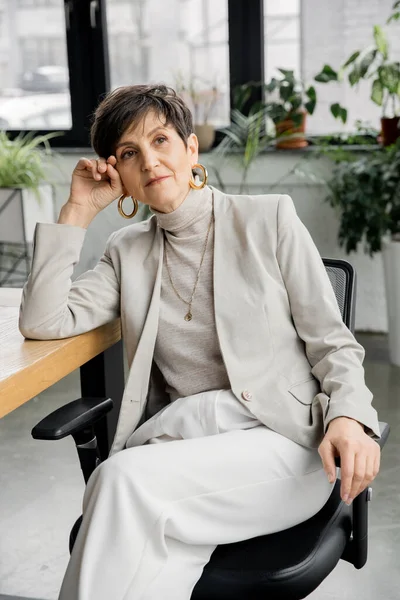 Nachdenkliche Frau mittleren Alters, erfahrene Unternehmerin, sitzend und wegschauend, Entscheidungsfindung — Stockfoto