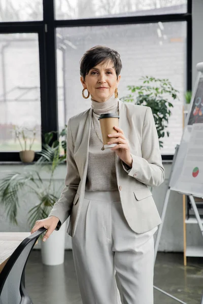 Successful middle aged businesswoman with takeaway drink looking at camera in office, portrait — Stock Photo