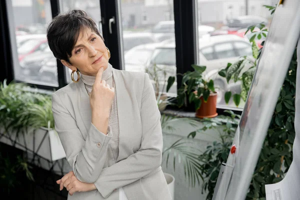 Thoughtful middle aged businesswoman looking at blurred flip chart in office, decision making — Stock Photo