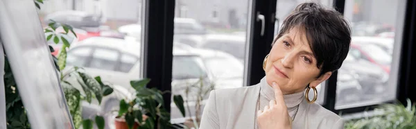Pensive middle aged entrepreneur thinking near flip chart on blurred foreground in office, banner — Stock Photo