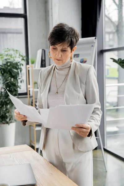 Seriöse Frau, Führungskraft, die am Arbeitsplatz im Büro steht und Papiere betrachtet — Stockfoto