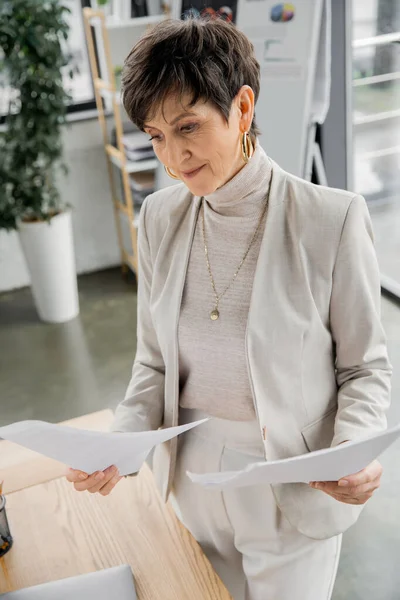 Concentrata donna d'affari di mezza età guardando i documenti in ufficio moderno, documenti, — Foto stock
