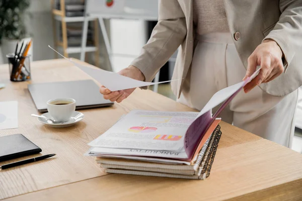 Cropped view of mature businesswoman looking at documents with graphs in modern office — Stock Photo