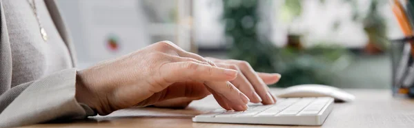 Partial view of middle aged businesswoman working in office and typing on keyboard, banner — Stock Photo