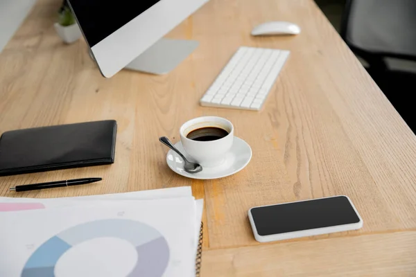 Computermonitor, Tastatur, Kaffeetasse, Notizbuch, Stift, Dokumente mit Infografik auf dem Schreibtisch — Stockfoto