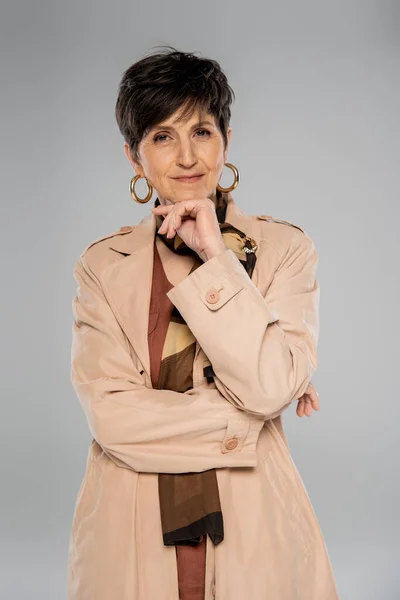 Mulher de meia-idade na moda e sorridente em cinza, casaco de trincheira, cachecol, brinco de argola, outerwear outonal — Fotografia de Stock