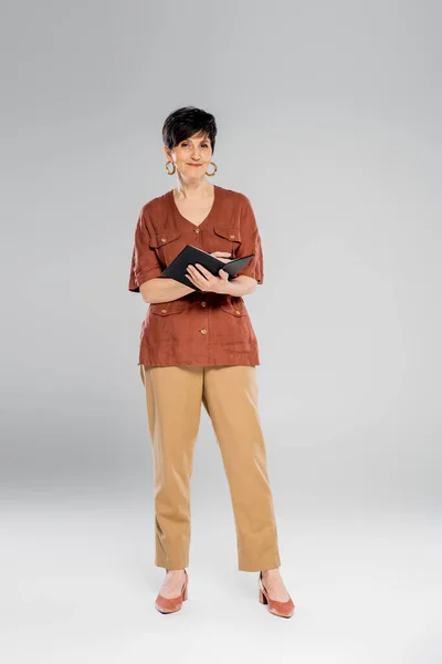 Mulher de negócios na moda com notebook em cinza, queda, moda sazonal, jaqueta marrom, calças bege — Fotografia de Stock