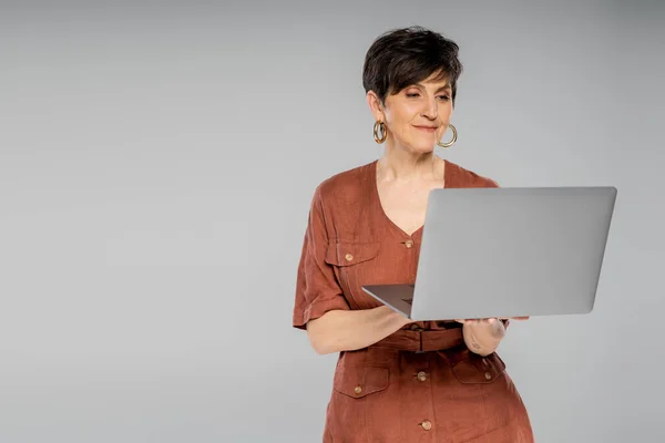 Femme d'affaires d'âge moyen en veste marron travaillant sur ordinateur portable sur gris, look automne tendance — Photo de stock