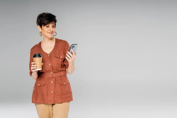 Mature businesswoman with smartphone and coffee to go on grey, fashion style, trendy look — Stock Photo