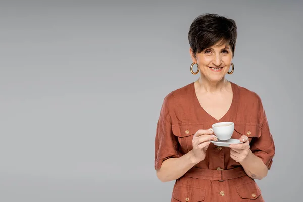 Brunette femme d'âge moyen avec tasse de café souriant à la caméra sur gris, look branché, style automne — Photo de stock