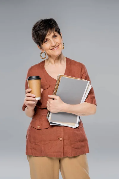 Femme d'affaires mature avec café à emporter et documents souriants sur gris, tendance de la mode d'automne — Photo de stock