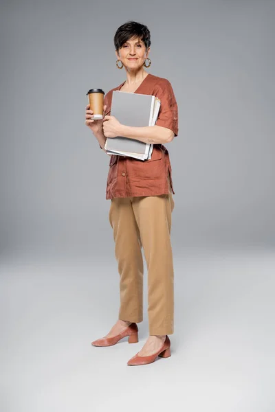 Middle aged businesswoman with documents, takeaway drink on grey, stylish autumn look, full length — Stock Photo