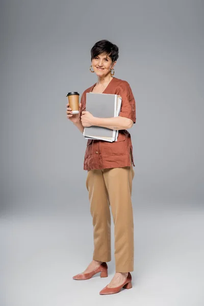 Trendy middle aged businesswoman with coffee to go and documents on grey, autumn fashion trend — Stock Photo