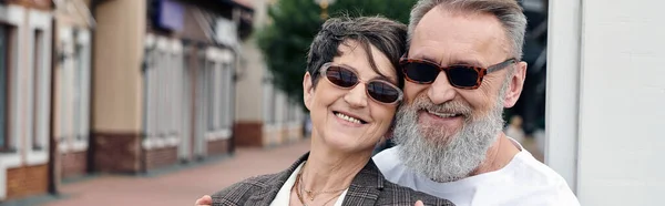 Heureux, couple âgé dans des lunettes de soleil souriant et regardant caméra, été, senior homme étreignant femme — Photo de stock