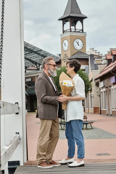 Felice coppia anziana in occhiali da sole, uomo guardando donna con fiori, estate, bouquet, romanticismo — Foto stock