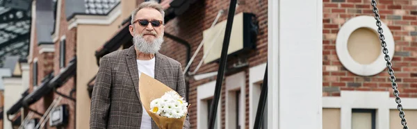 Hombre mayor con barba y gafas de sol con ramo de flores, de pie en la calle urbana, pancarta — Stock Photo