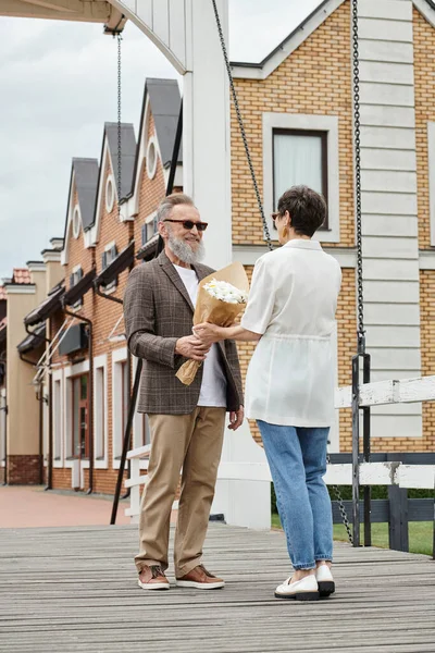 Heureux homme âgé avec barbe et lunettes de soleil donnant bouquet à la femme sur la rue urbaine, date, romance — Photo de stock