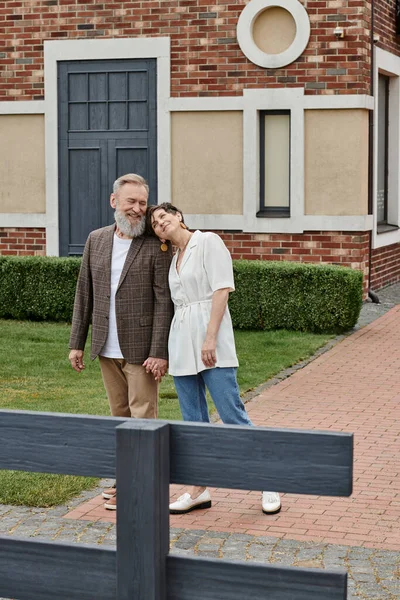 Веселая пожилая пара, женщина, опирающаяся на плечо мужчины, стоящая рядом с домом, любовь, романтика, свидание — стоковое фото