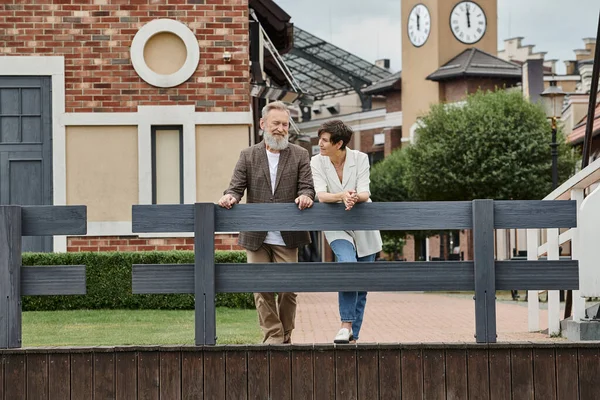 Glückliches älteres Paar, Frau schaut Mann an, steht am Zaun, urbane Kulisse, alternde Bevölkerung — Stockfoto