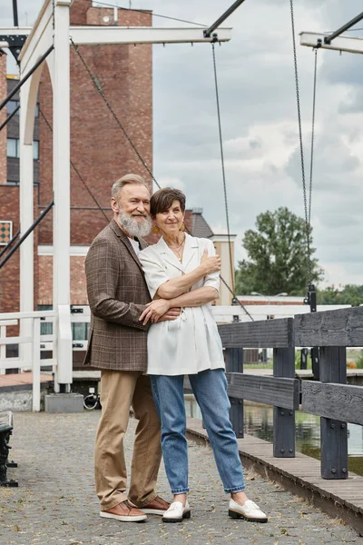 Влюбленная пара, счастливая пожилая пара обнимается, стоя вместе на улице, бородатый мужчина, женщина, свидание — стоковое фото