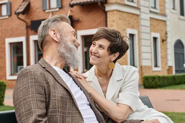 Happy elderly woman looking at bearded man, romance, husband and wife, urban background, love — Stock Photo