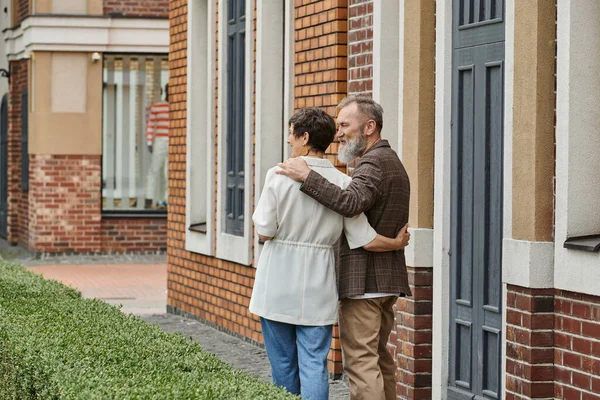 Senior man with beard hugging woman, husband and wife near building, urban, street, happy, romance — Stock Photo