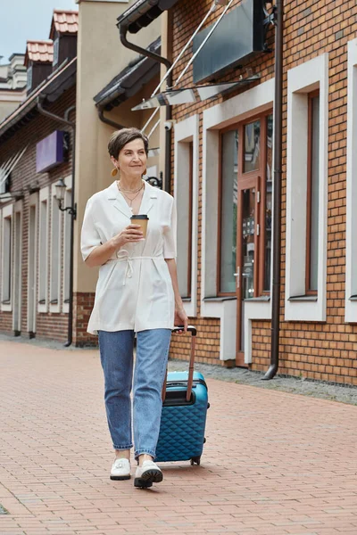 Glückliche ältere Frau hält Pappbecher in der Hand und geht mit Gepäck, Coffee to go, urbanem Lebensstil — Stockfoto