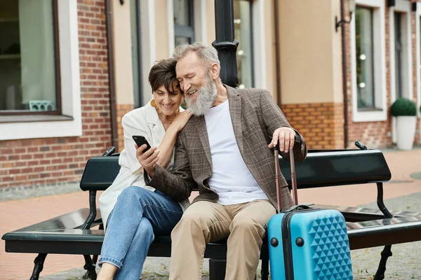 Älteres paar, glücklicher älterer mann mit smartphone, sitze mit frau auf bank, gepäck, gerät — Stockfoto