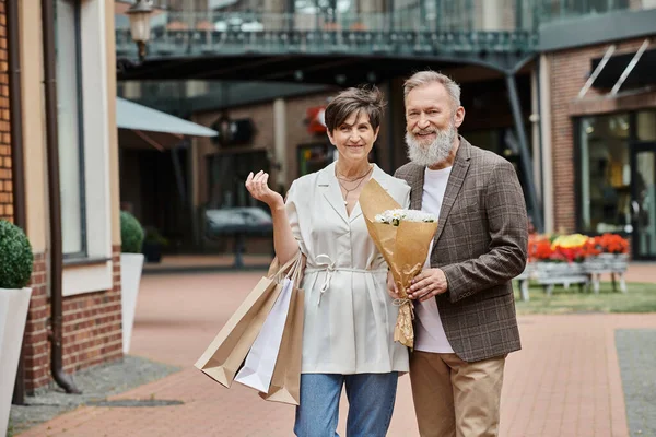 Happy elderly couple, shopping, bouquet of flowers, romance, active seniors, aging population, city — Stock Photo