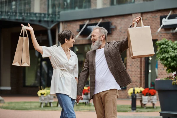 Aufgeregtes und älteres Paar mit Einkaufstaschen, Lebensstil in der Stadt, glücklicher Mann und Frau, älteres Leben — Stockfoto