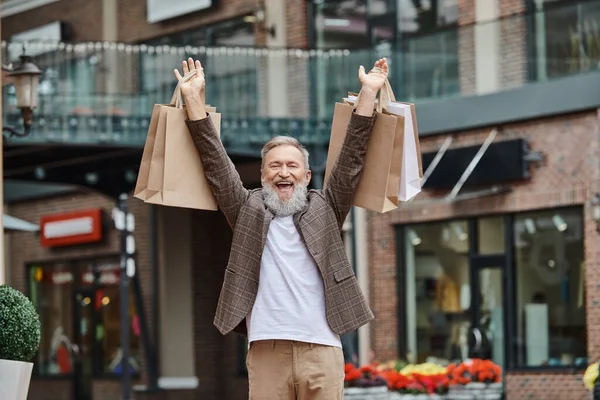 Збуджений і бородатий чоловік ходить з сумками, старшим життям, міською вулицею, стильним вбранням — стокове фото