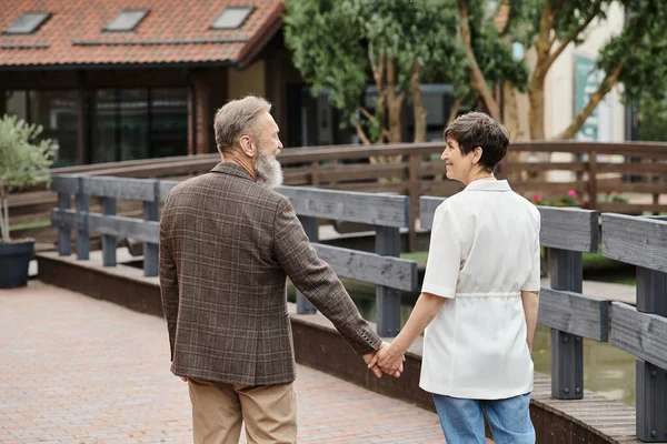 Mujer feliz y hombre barbudo tomados de la mano, mirándose, cita, romance, pareja de ancianos - foto de stock