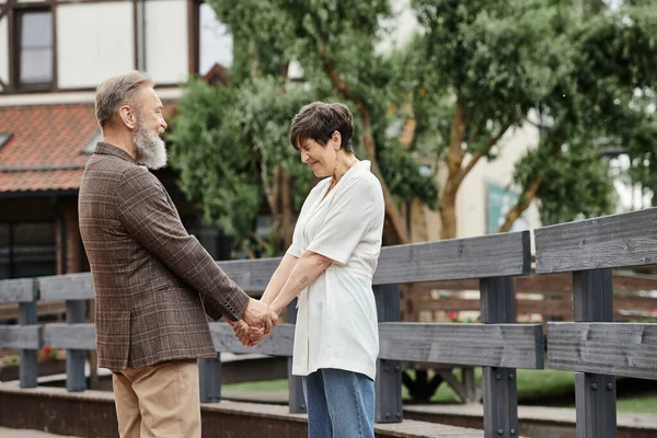 Donna e uomo barbuto che si tiene per mano, guardarsi l'un l'altro, appuntamento, romanticismo, felice coppia anziana — Foto stock