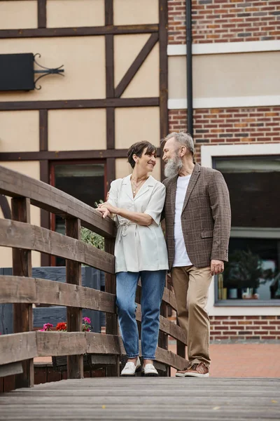 Heureux barbu homme et femme regardant l'autre, couple âgé, debout près du pont, romance — Photo de stock