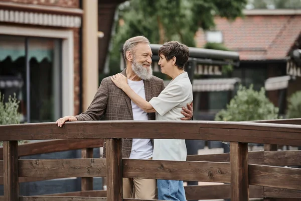 Romantica coppia anziana in piedi insieme sul ponte di legno e si abbracciano, amore anziano, legame — Foto stock