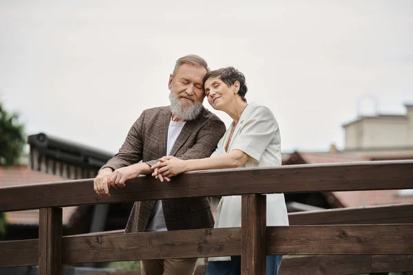 Happy couple standing together on bridge, elderly love, bearded man and woman with closed eyes — Stock Photo