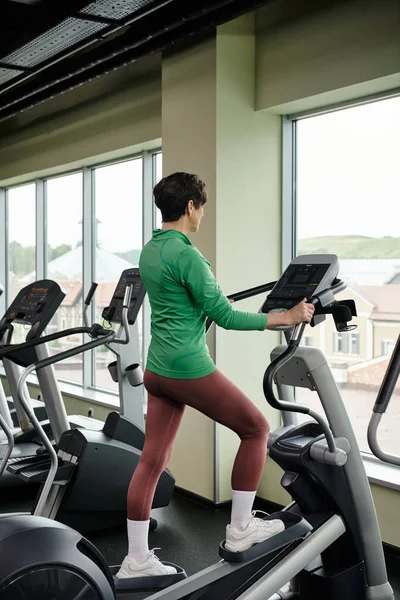 Senior activo, mujer de edad avanzada en la ropa deportiva de ejercicio en el gimnasio, utilizando la máquina de ejercicio paso a paso, el deporte - foto de stock