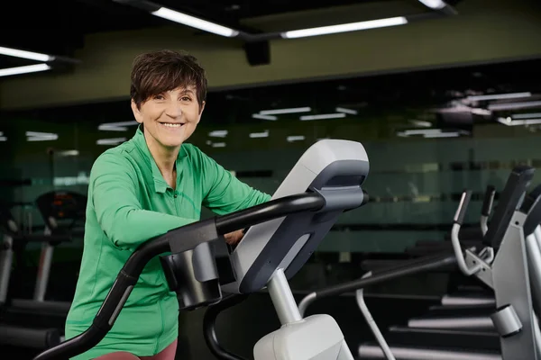 Senior actif, femme âgée heureuse en vêtements de sport faisant de l'exercice dans la salle de gym, machine d'exercice, sport — Photo de stock