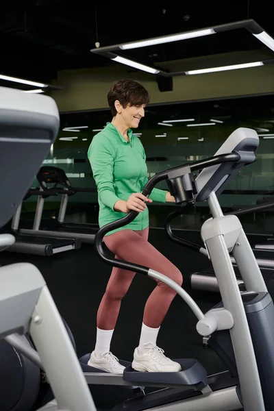 Senior actif, femme âgée heureuse en vêtements de sport faisant de l'exercice dans la salle de gym, en utilisant une machine d'exercice pas à pas — Photo de stock